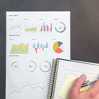 Person's hand on a notebook with a page of graphs and data measurement placed beside the notes