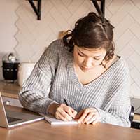 Woman writing notes next to laptop Woman writing notes next to laptop